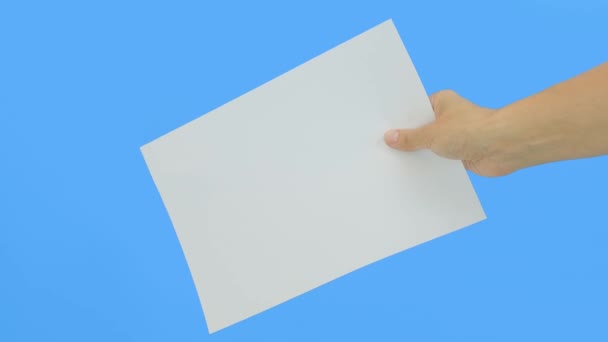 Eine Hand hält ein weißes leeres Blatt Papier A4 mit Kopierraum vor blauem Hintergrund — Stockvideo