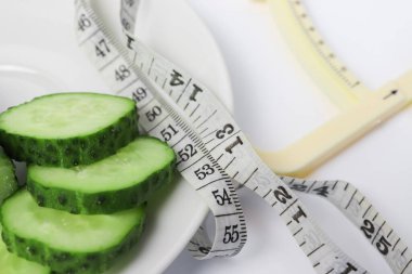 Taze yeşil dilimlenmiş salatalık, bir mezura ve beyaz arka planda kalibreli zayıflatma ve kilo verme konsepti..