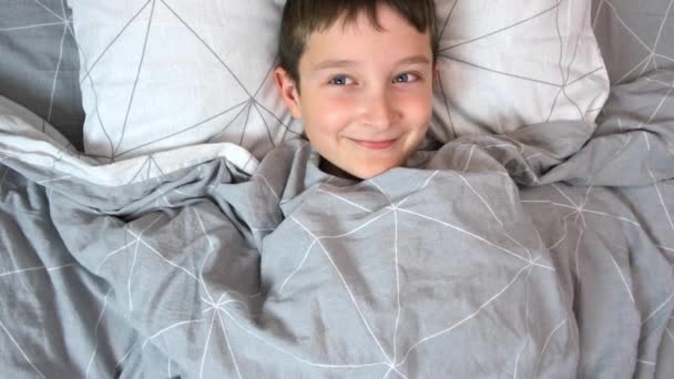 Ένα χαμογελαστό καυχησιάρικο αγόρι ξαπλωμένο στο κρεβάτι το πρωί, χαρούμενη παιδική ιδέα — Αρχείο Βίντεο