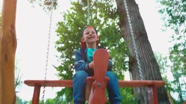 Güneş ışığı altında bir parkta bir uçak şeklinde ahşap bir salıncak üzerinde boy mutlu gülümseyerek. Bir çocuk bir salıncakta eğleniyor