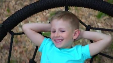 Mavi t-shirt yalanlar üzerine ellerini başını bakar, gülümser ve kamera arkasında yuvarlak bir vuruşta mavi gözlü beş yaşındaki çocuk çocuk, salıncakta yalan dinleniyor