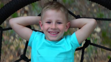 Mavi t-shirt yalanlar üzerine ellerini başını bakar, gülümser ve kamera arkasında yuvarlak bir vuruşta mavi gözlü beş yaşındaki çocuk çocuk, salıncakta yalan dinleniyor