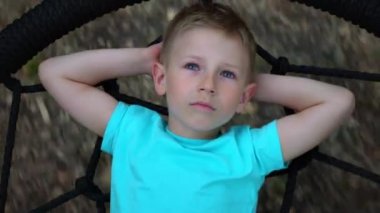 Mavi gözlü beş yaşındaki çocuk yalan atar ellerini kafasının arkasına kadar yuvarlak bir salıncak üzerinde gökyüzü ve rüyalar, çocuk yukarı bakar dinlenme, salıncakta yalan