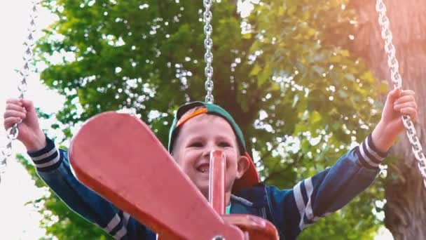 Güneş ışığı altında bir parkta bir uçak şeklinde ahşap bir salıncak üzerinde boy mutlu gülümseyerek. Bir çocuk bir salıncak, yavaş hareket eğleniyor — Stok video