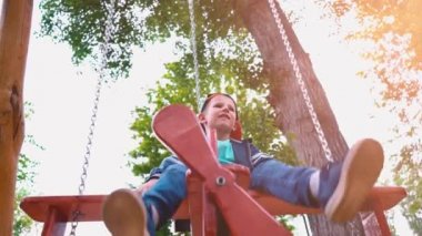 Güneş ışığı altında bir parkta bir uçak şeklinde ahşap bir salıncak üzerinde boy mutlu gülümseyerek. Bir çocuk bir salıncak, yavaş hareket eğleniyor