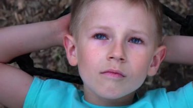 Beş yaşında mavi gözlü çocuk t-shirt yuvarlak salıncakta yatıyor, ellerini başının arkasına kadar atar, gökyüzü ve rüyalar baktı mavili çocuğa çocuk, salıncakta çocuk rüyalar yalan dinleniyor