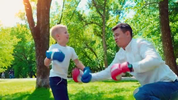 Father and son in boxing gloves play boxing on the lawn near the house — Stock Video