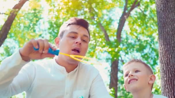 Vater mit seinem Sohn, der Seifenblasen pustet, lustiger Familienspaß, ein Kind, das Spaß mit seinem Vater hat — Stockvideo