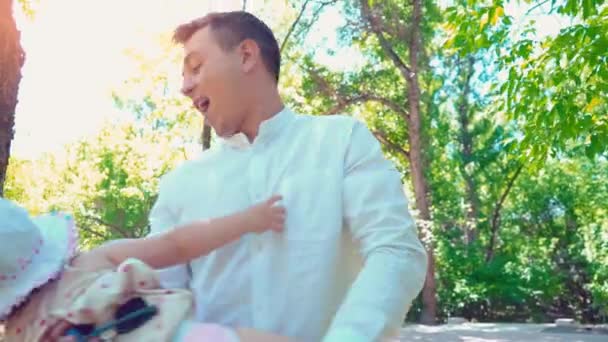 Młody ojciec szczęśliwy posiada małą córką z jego rąk i ją skręca go w parku lato, grając z dzieckiem — Wideo stockowe