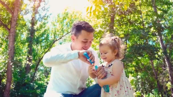 Far blåser såpbubblor och lilla dotter fångar dem i parken, familj livsstilskoncept — Stockvideo