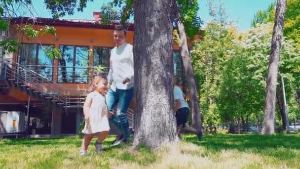 Mladý otec s dětmi kolem stromu poblíž domu rostuschego, tati, syn a dcerka baví ve dvoře — Stock video