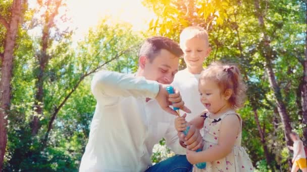 父亲吹肥皂气泡为儿子和小女儿在公园, 生活方式家庭概念 — 图库视频影像
