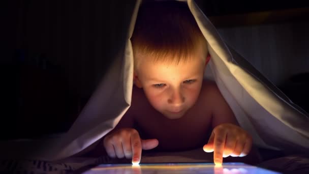 Ung blond pojke under täcker spelar på tablett datorspel. — Stockvideo