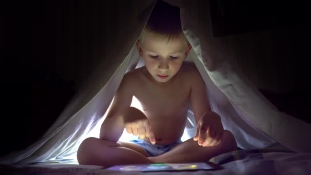 Молодой блондин под одеялом играет на планшете в компьютерную игру . — стоковое видео