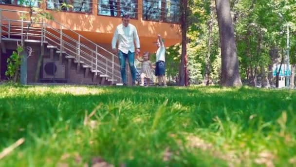 Vater mit Sohn und kleiner Tochter im grünen Gras am Haus händchenhaltend — Stockvideo