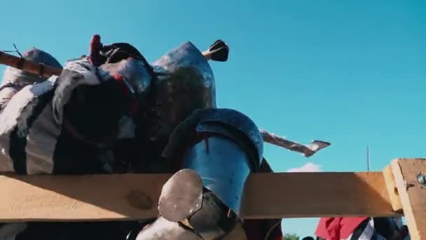 Knight Tournament. Strong men in steel armor with weapons in hand are fighting near a wooden fence against the blue sky — Stock Video