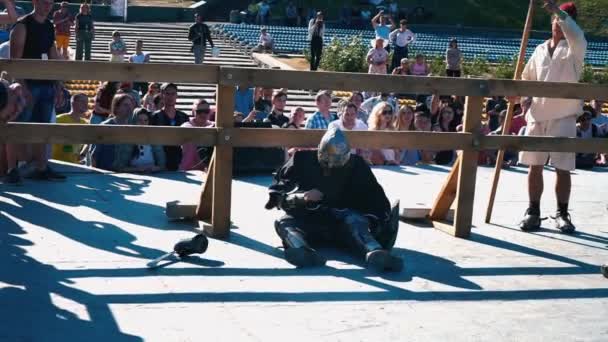 Ucrania, Kiev, 9 de junio de 2018. Torneo de Caballeros. El caballero derrotado, sentado cerca de la valla de madera, ayuda a quitar el casco de hierro — Vídeo de stock
