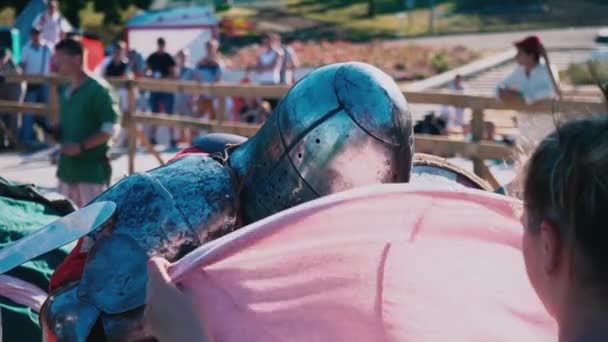 Oekraïne, Kiev, 9 juni 2018. Ridder toernooi. Een vrouw golven een roze sjaal over een vermoeide ridder leunend tegen een houten hek — Stockvideo