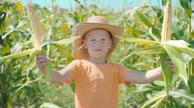 Hasır şapkalı bir çocuk bir tarlasında oynarken, çocuk Mısır koçanı koruyor ve kendini bir kovboy olarak sunar