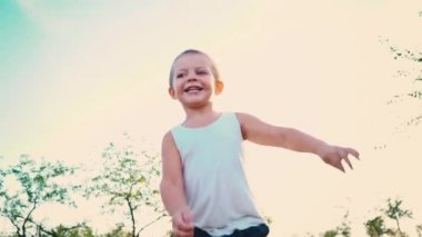 beyaz bir t-shirt 4 yaşındaki çocuk gülüyor, Çocuk gökyüzüne karşı atlar. Doğa arka plan üzerinde bir etkin çocuk portresi.