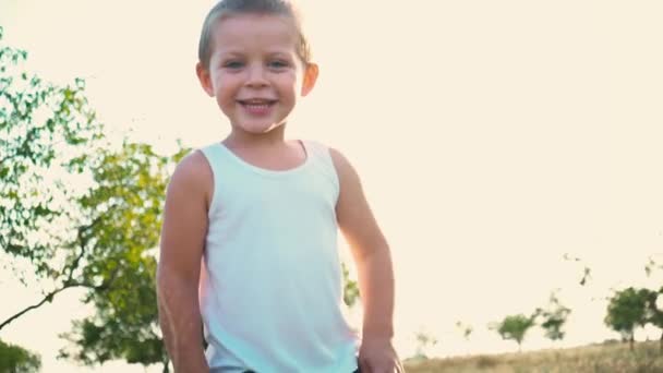 Porträt eines fröhlichen aktiven Kindes vor einem Hintergrund der Natur. kleiner Junge lächelt in die Kamera. Glückliche Kindheit. — Stockvideo