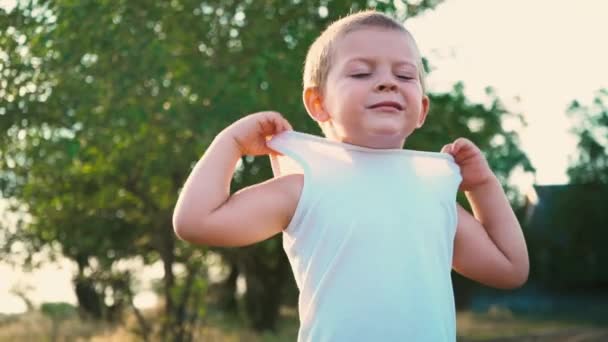 Porträt eines fröhlichen aktiven Kindes, schüchternes Kind versteckt einen Teil des Gesichts unter einem weißen T-Shirt — Stockvideo