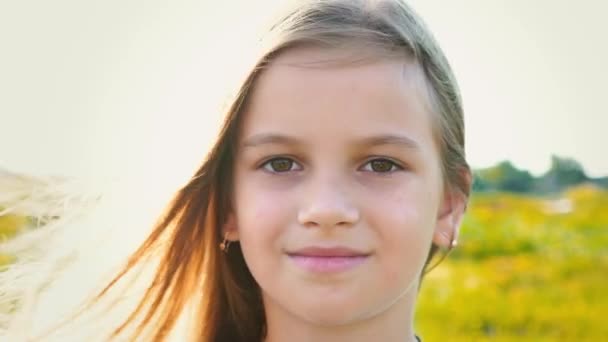 Портрет привлекательной маленькой девочки с большими карими глазами на фоне природы с развивающимися волосами — стоковое видео