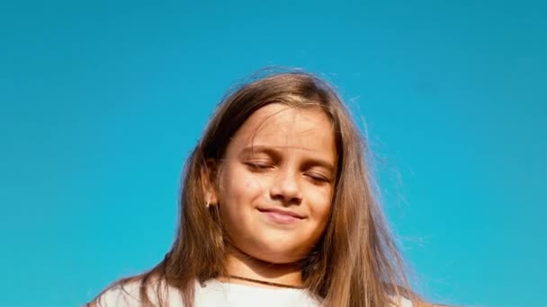 Retrato de una niña de pelo largo con los ojos cerrados contra el cielo azul, el niño sueña — Vídeos de Stock