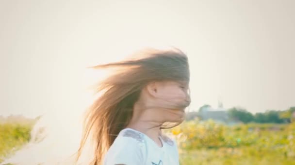 Una niña atractiva con el pelo largo que fluye tuerce su cabeza en diferentes direcciones, el viento desarrolla el pelo largo del niño — Vídeo de stock