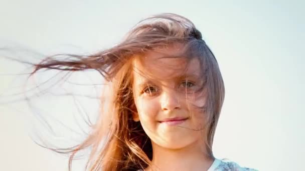 Портрет привлекательной маленькой девочки с большими зелеными глазами с развивающимися волосами на фоне ясного неба, девчушка с длинными волосами — стоковое видео