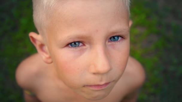 Retrato close-up de um menino de olhos azuis olhando diretamente para a câmera, um olhar penetrante de uma criança de 6 anos, vista de cima — Vídeo de Stock