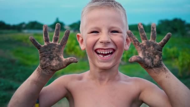 Un niño feliz muestra sus manos sucias de la tierra y se ríe, un niño manchado en el barro, un pasatiempo de la infancia feliz — Vídeos de Stock