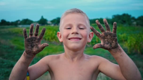 Šťastné dítě ukazuje jeho ruce špinavé od země a smích, chlapec namazal v bahně, veselé dětství zábava — Stock video