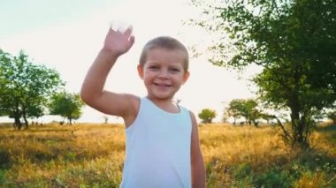Kameraya bakarak onun elini sallayarak beyaz tişört utangaç 4 yaşındaki çocuk, küçük çocuk selamlar, yaz doğa çerçevede çocuk gönderir