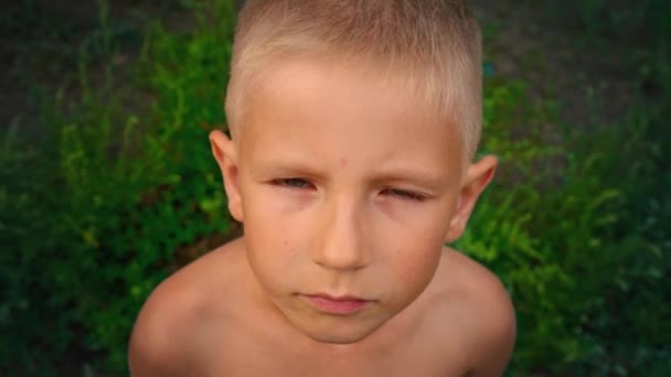 Close-up πορτρέτο του ένα μπλε-eyed αγοράκι βλέπει απευθείας την κάμερα και προσπαθεί να χαμογελάσει, ένα διαπεραστικό βλέμμα ενός παιδιού 6-year-old, άποψη από ψηλά — Αρχείο Βίντεο