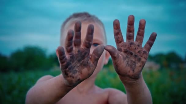 Щаслива дитина показує свої руки брудними з землі, хлопчик розмазаний у бруді, веселе дитинство — стокове відео