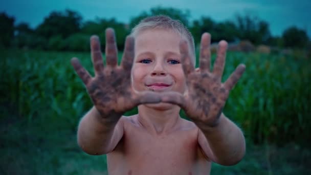 Un niño feliz muestra sus manos sucias desde el suelo, un niño manchado en el barro, un pasatiempo de la infancia feliz — Vídeos de Stock