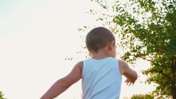 Четырехлетний мальчик в белой футболке смеется и протягивает руки. Портрет веселого активного ребенка на природе . — стоковое видео