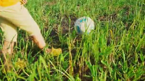 Un niño patea una pelota de fútbol con los pies en la hierba verde alta en el campo, vista de las piernas desde el lado — Vídeo de stock