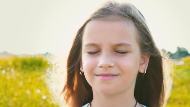 Портрет привлекательной маленькой девочки с большими глазами на фоне природы с развивающимися волосами, девочка закрывает лицо руками от ветра — стоковое видео