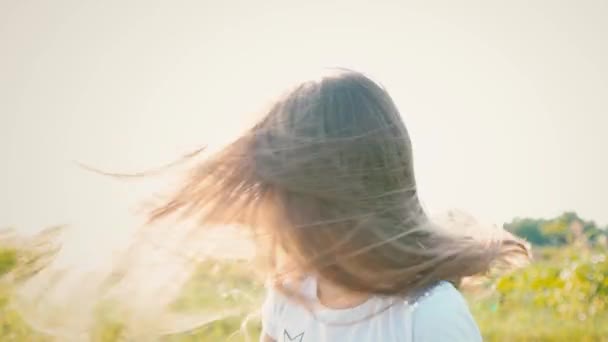 Una niña atractiva con el pelo largo que fluye tuerce su cabeza en diferentes direcciones, el viento desarrolla el pelo largo del niño — Vídeos de Stock
