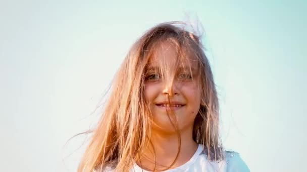 Atraktivní holčička s dlouhou splývavou srstí kroutí hlavou v různých směrech, dívka si hraje s její vlasy ve větru, vítr se vyvíjí dlouhé vlasy dítěte — Stock video