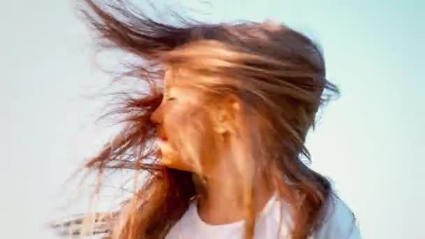Приваблива маленька дівчинка з довгим волоссям крутить голову в різних напрямках, дівчинка грає з волоссям на вітрі, вітер розвиває довге волосся дитини — стокове відео