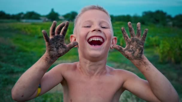 Un niño feliz muestra sus manos sucias de la tierra y se ríe, un niño manchado en el barro, un pasatiempo de la infancia feliz — Vídeos de Stock