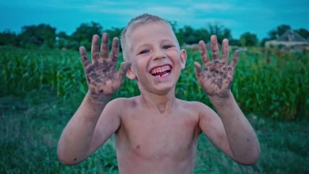 Un niño feliz muestra sus manos sucias de la tierra y se ríe, un niño manchado en el barro, un pasatiempo de la infancia feliz — Vídeos de Stock