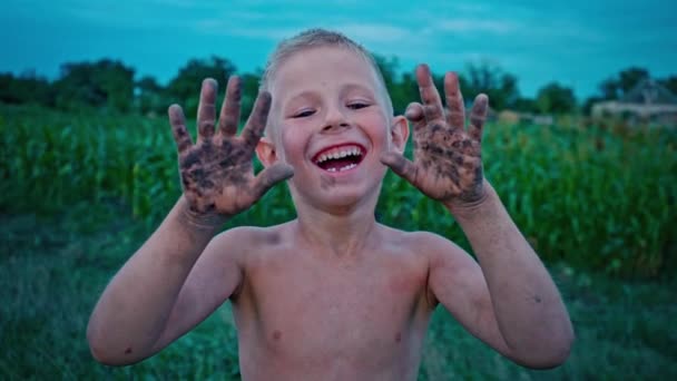 Un niño feliz muestra sus manos sucias de la tierra y se ríe, un niño manchado en el barro, un pasatiempo de la infancia feliz — Vídeos de Stock