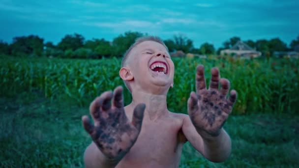 Ένα χαρούμενο παιδί δείχνει τα χέρια του βρώμικα από τη γη και τα γέλια, ένα αγόρι αλείψει στη λάσπη, merry προορισμών — Αρχείο Βίντεο