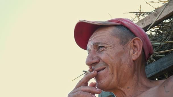 Retrato de un trabajador fumador en el contexto de una escena rural. Un granjero con gorra fuma un cigarrillo — Vídeo de stock