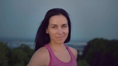 Şehrin arka plan üzerinde çekici bir sporcumuz portresi. Sportif bir yapı olan sevimli kadın kameraya bakıyor. Uzun saçlı esmer günbatımı uzakta fonunda poz