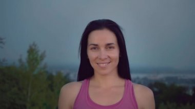 Şehrin arka plan üzerinde çekici bir sporcumuz portresi. Sportif bir yapı olan sevimli kadın kameraya bakıyor. Uzun saçlı esmer günbatımı uzakta fonunda poz